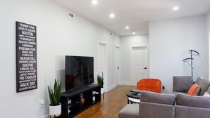 Ein modernes Wohnzimmer mit einem Flachbildfernseher, einem grauen Sofa, einem orangefarbenen Sessel und einer schwarzen Unterhaltungseinheit.