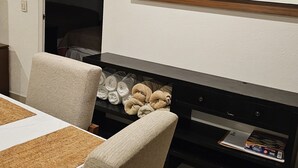 A dining area with a table set for two, a chair, a wooden cabinet with towels, and a mirror on the wall.