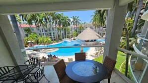 A balcony with a view of a pool, wicker furniture, and a thatched-roof structure.