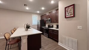 Una cocina moderna con armarios de madera oscura, una isla grande y un comedor con sillas de mimbre.