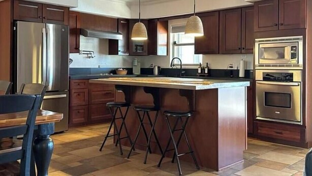 Een moderne keuken met donkere houten kasten, roestvrijstalen apparatuur en een centraal eiland met barkrukken.