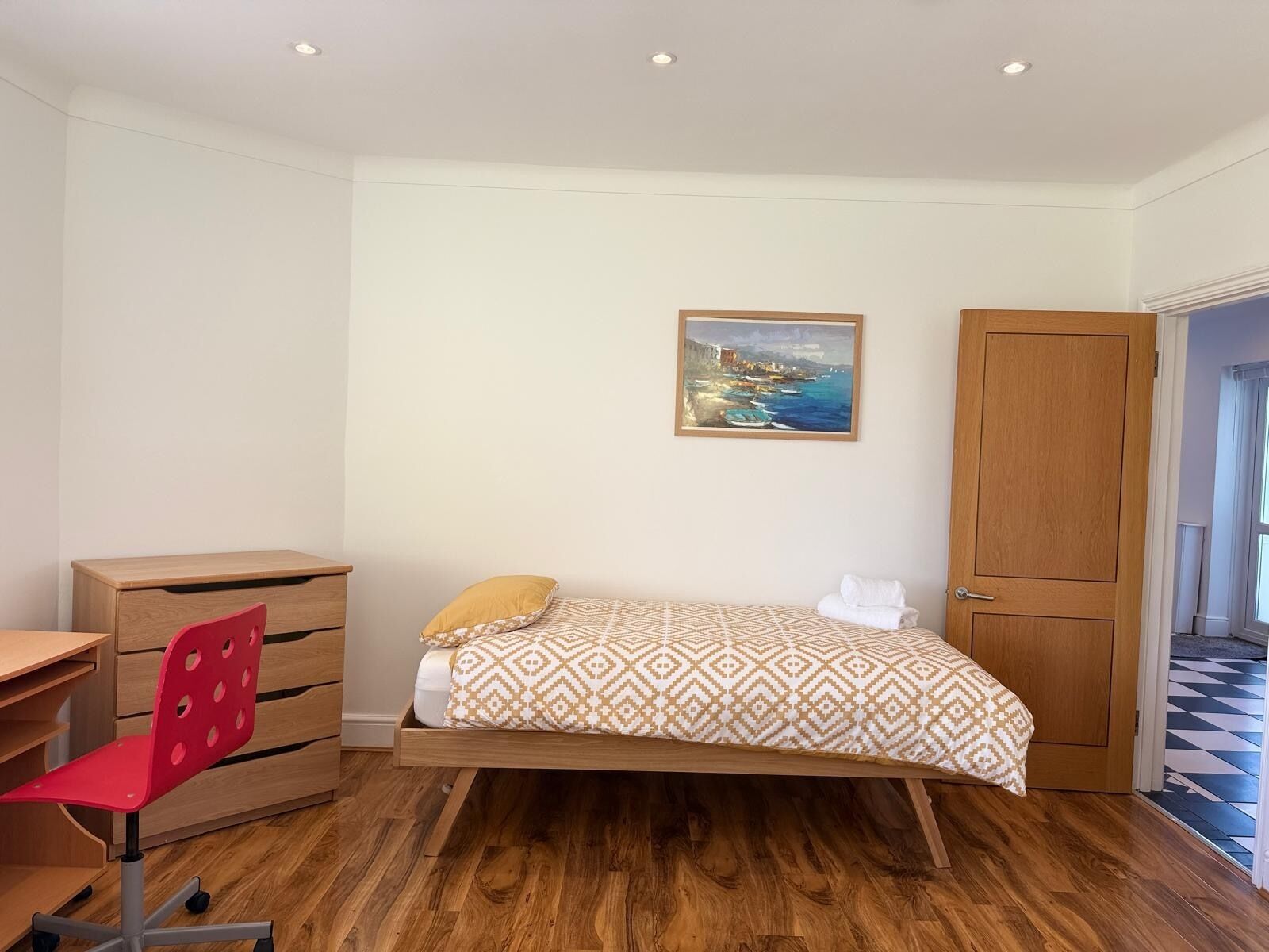 Un dormitorio con una cama, un escritorio, una silla, un armario y un cuadro en la pared.