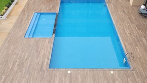 Una piscina sul tetto con un solarium in legno, circondata da poltrone relax e un moderno palazzo condominiale sullo sfondo.