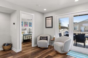 A modern interior with a wooden floor, a white armchair, a framed sign, and a view through a glass door.