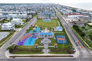 An aerial view of a residential area with houses, a road, and a playground with a circular fountain.