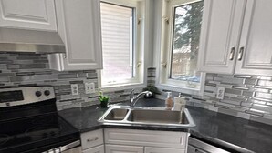 Una cocina con armarios blancos, horno de acero inoxidable, pileta doble y una ventana.
