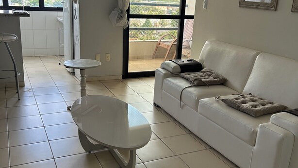 Un salon moderne avec un canapé blanc, une petite table ronde et un balcon offrant une vue sur la ville.