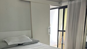 Un lit bien fait, avec du linge de lit blanc et une serviette pliée, une fenêtre avec des rideaux et un climatiseur au plafond.