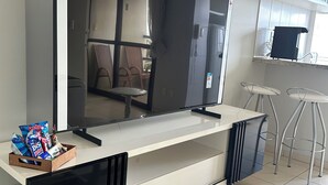 Une cuisine moderne équipée d’un grand téléviseur à écran plat, d’une machine à café et d’un petit coin salon avec des chaises.