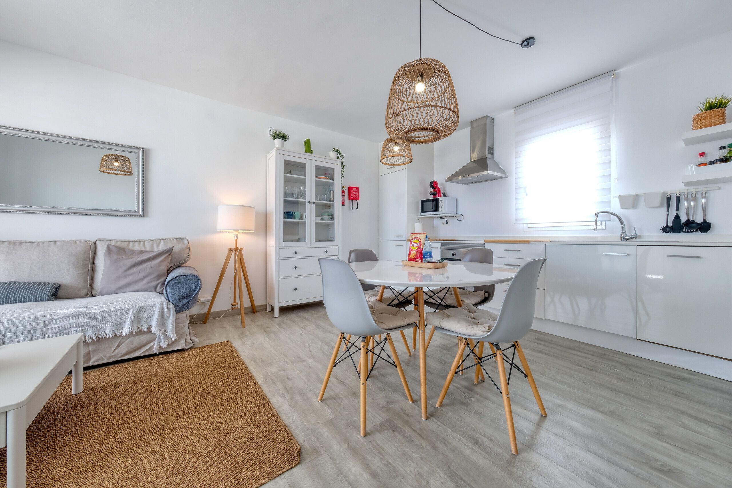 A modern kitchen with white cabinets, a dining table with chairs, and a hanging light fixture.