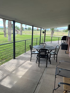 A covered patio with a table and chairs, a grill, and a view of a grassy field. - Farm Stay Cozy 2-bedroom guest house on farm in Hotchkiss (Hotchkiss)
