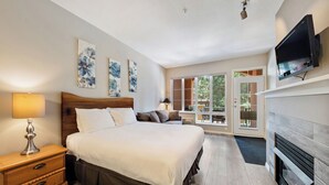 Quarto com cama grande, mesa de cabeceira de madeira, abajur e televisão fixada na parede.