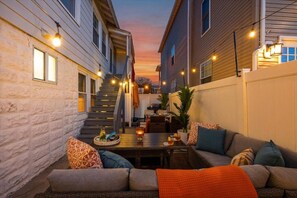 Un patio exterior acogedor con mesa, sillas y luces colgantes.