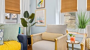 A cozy living room with a wicker chair, a potted plant, and a framed picture on the wall.