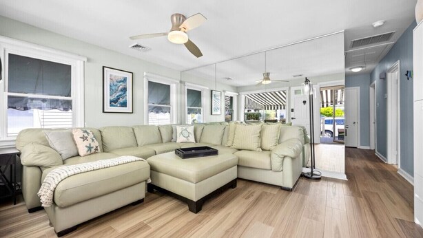 A modern living room with a sectional sofa, a ceiling fan, and a large window. - 3BR Home - Close to Beach - Backyard Oasis (Margate City)