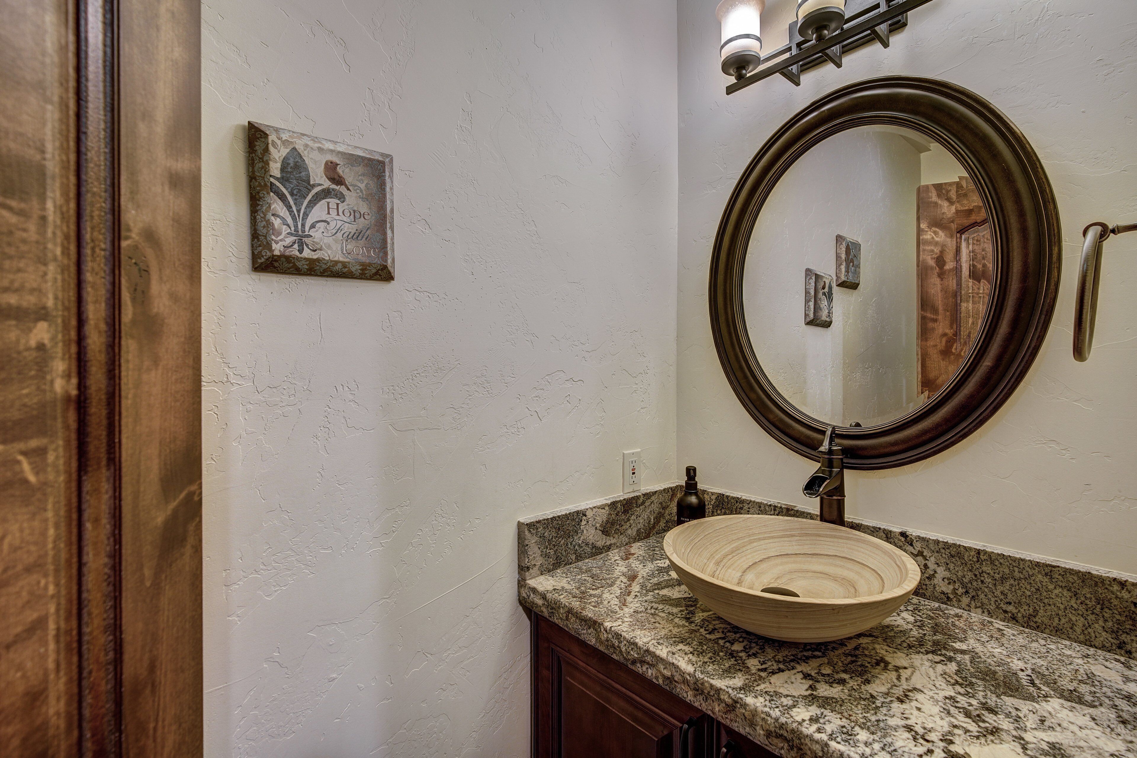 A bathroom with a wooden vanity, a round mirror, and a wall-mounted light fixture.