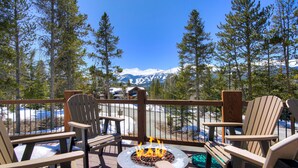 Una terraza con sillas Adirondack, un pozo de fuego y vistas a montañas nevadas.