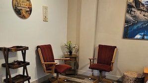 Ein Zimmer mit Holzboden, zwei roten Stühlen, einem kleinen Tisch, einer Wandregal und einem Gemälde einer Berglandschaft.