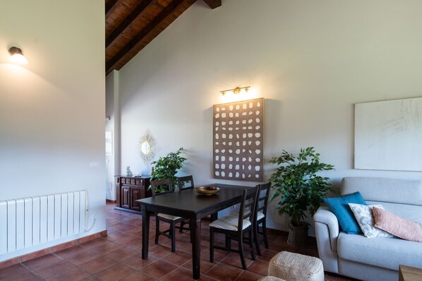 A dining area with a table and chairs, a radiator, a decorative wall panel, and a sofa with cushions.