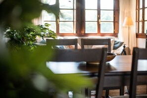 A dining area with wooden furniture, a potted plant, and large windows allowing natural light.