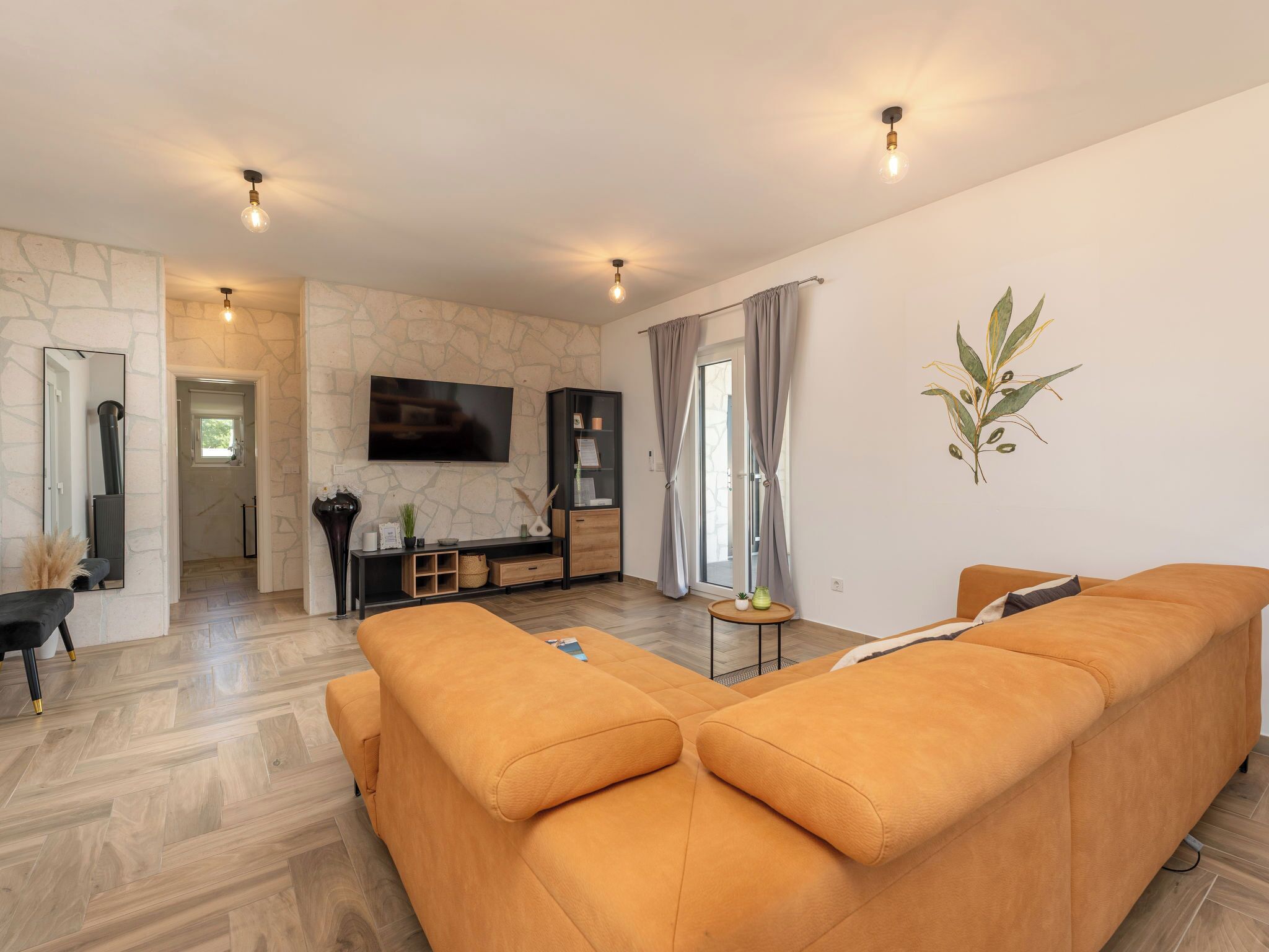 Un salon moderne avec un canapé d’angle, un téléviseur à écran plat, un mur en pierre et un style de décoration minimaliste.