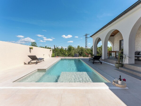 Une piscine avec des chaises longues, un patio couvert et un mur en pierre.