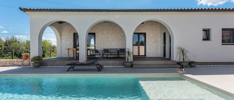 Une maison moderne dotée d’une piscine, de trois porches en arc de cercle et de mobilier d’extérieur.