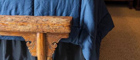 A bedroom with a wooden bed frame, a blue bedspread, and a wooden nightstand with a lamp.