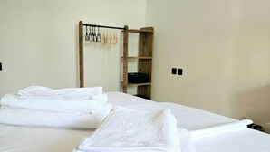 Una cama bien hecha con toallas blancas dobladas y un estante de madera con un objeto negro.