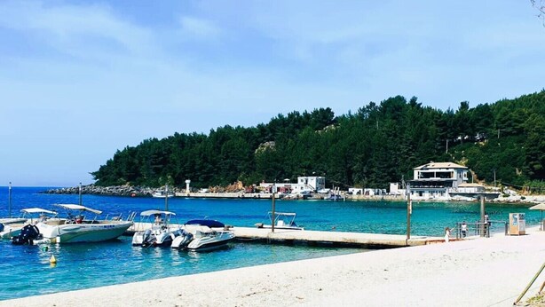Una marina costera con barcos amarrados, una playa de arena y una colina con edificios.