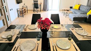 Un comedor con una mesa larga dispuesta para seis personas, un sofá y un televisor al fondo.