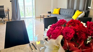 Una sala de estar moderna con un sofá gris, almohadones amarillos y una mesa de comedor preparada con un plato, cubiertos y un vaso de agua.