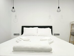 Ein ordentlich bezogenes Bett mit weißen Leinen und Handtüchern, ein schwarzer Kopfteil und zwei Pendelleuchten.
