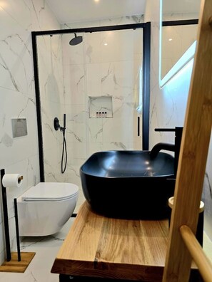 Ein modernes Badezimmer mit Marmorwand, Waschbecken in Schwarz und Toilette in Weiß.