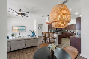 Une cuisine moderne avec des meubles de couleur bois foncé, un îlot central et un coin repas comprenant une table ronde et des chaises en osier.