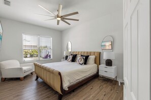 A bedroom with a bed, a chair, a bedside table, a lamp, a ceiling fan, and a window with blinds. - Luxury Escapes Home W/ Heated Pool  Near IMG & Siesta Key  Beach (Bradenton)