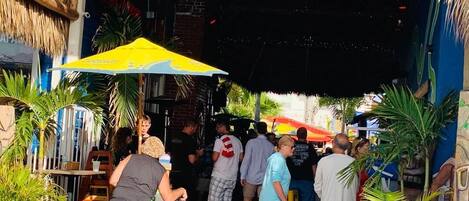A crowded outdoor area with people, a yellow umbrella, and potted plants.