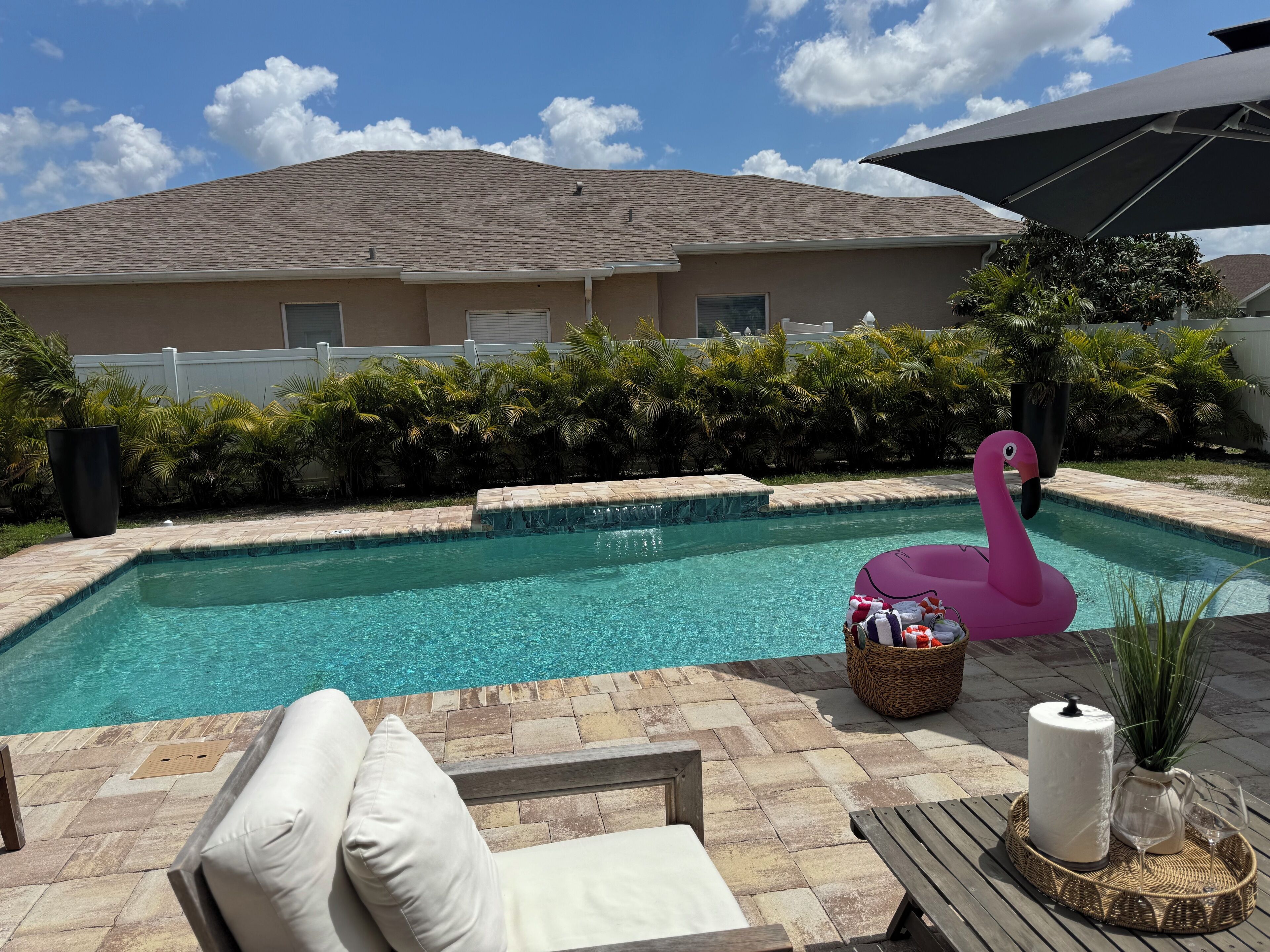 Une piscine avec un flotteur en forme de flamant rose, un panier en osier et une bougie sur une table.