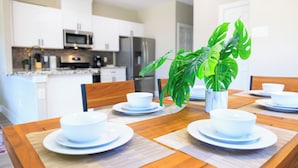 A dining table set with white bowls and plates, a potted plant, and a modern kitchen in the background.