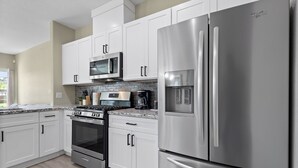 A modern kitchen with white cabinets, stainless steel appliances, a microwave, oven, and a refrigerator.