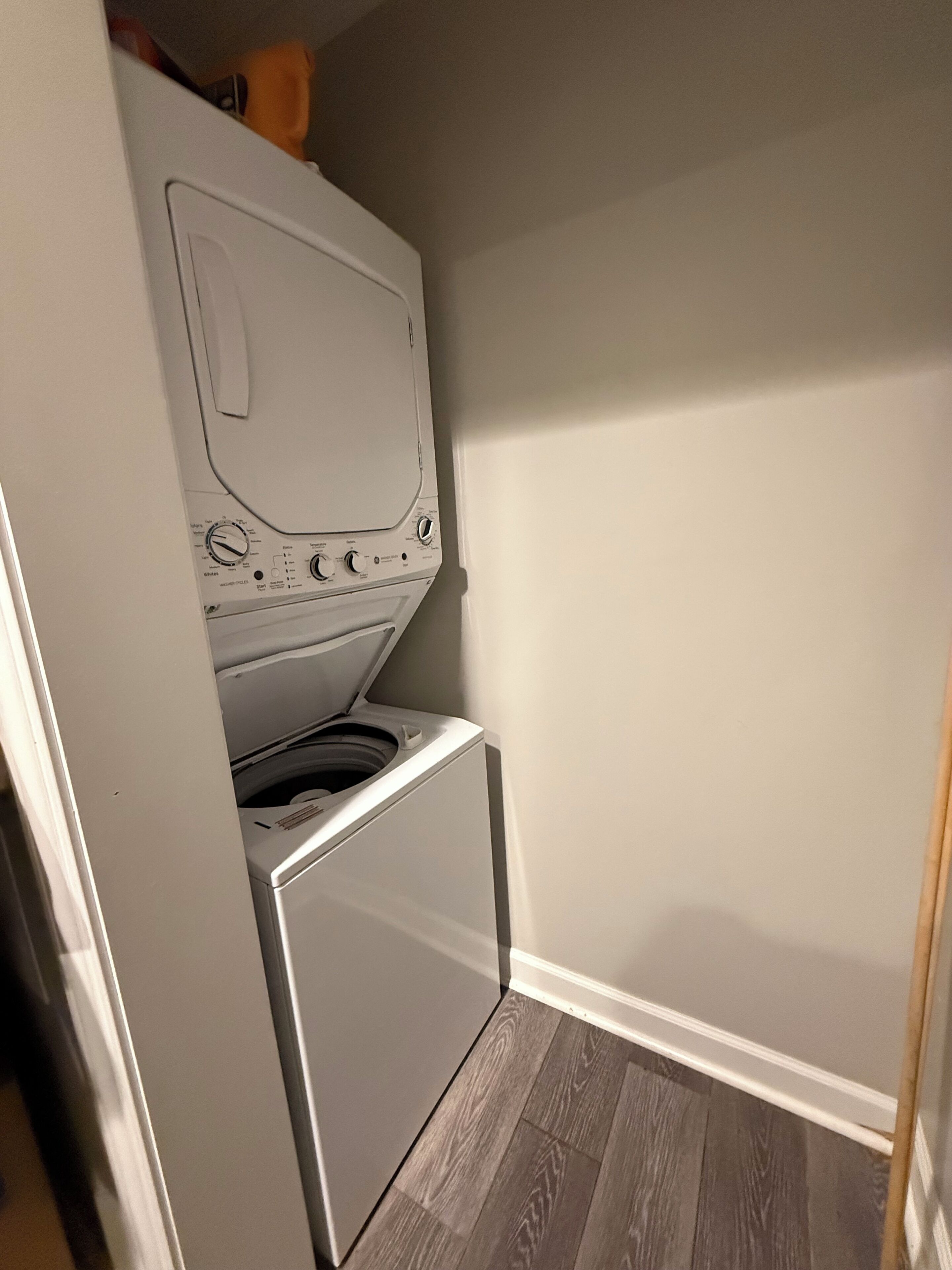 Een kleine wasruimte met een voorlader wasmachine en droger, houten vloeren en een effen muur.