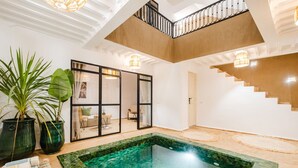 Un interior moderno con un balcón con cerramiento de vidrio, una pequeña piscina con mosaicos y una escalera con detalles de madera.