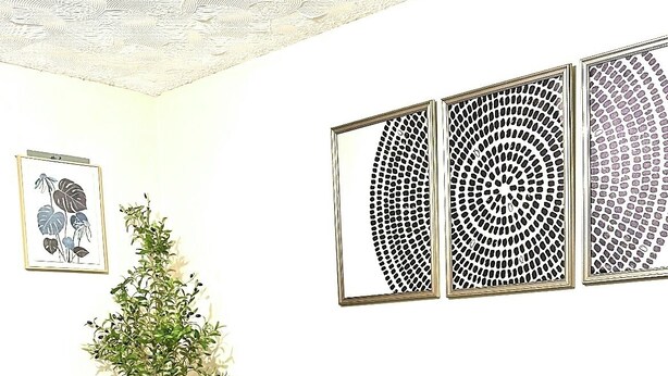 Uma sala de estar com um sofá cinzento, almofadas azuis e laranja, uma mesa de centro de madeira e uma pequena planta. Há obras de arte emolduradas na parede e um vaso com planta ao lado do sofá.