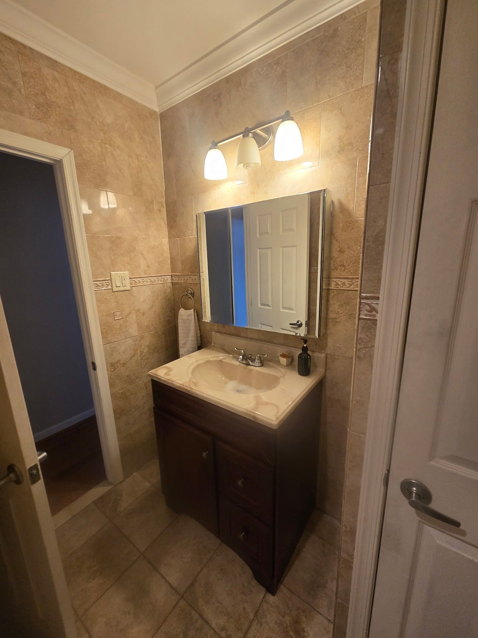 A bathroom with a beige sink, dark wooden vanity, and a mirror with three lights.
