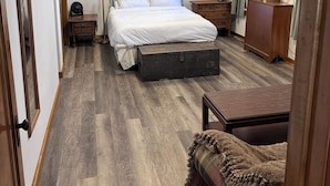 A hotel room with a bed, bedside table, dresser, and a large suitcase. - Beautiful Century old Apartments-Apt B (Algoma)
