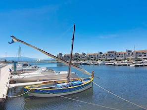 A marina with boats docked, a wooden pier, and buildings in the background.