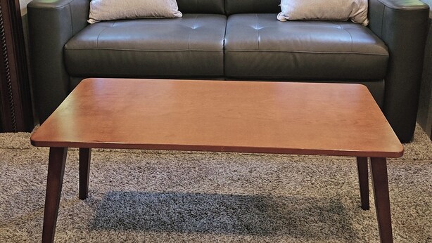 Ein dunkelbraunes Ledersofa mit zwei weißen Kissen und einem Holztisch davor.