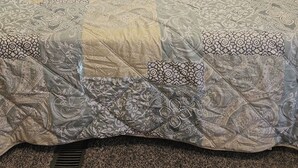 Ein Bett mit gesteppter Bettdecke und zwei Kissen, ein Fenster mit Vorhängen und ein Kopfteil.