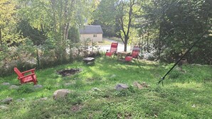Ein Garten mit einem kleinen Haus, einer Feuerstelle und roten Stühlen.