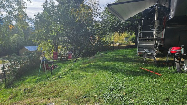 Un espace extérieur recouvert d’herbe, avec une échelle, un conteneur rouge et une chaise en métal.